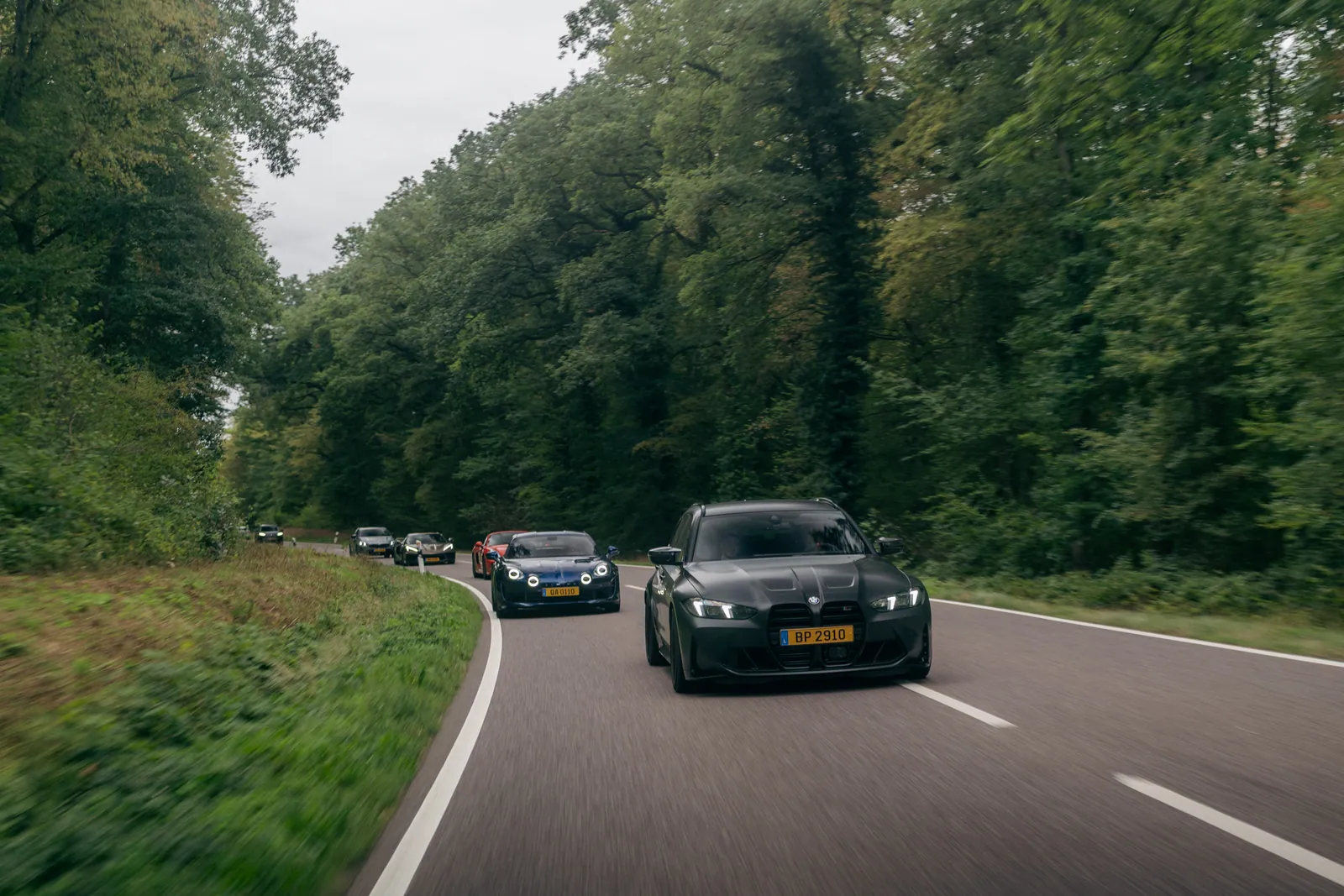 Cars driving in convoy on a tree-lined road